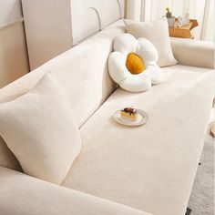 a white couch with two pillows and a plate on the sofa's arm rest