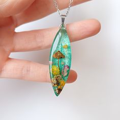 a hand holding a necklace with an image of flowers and mushrooms on it's side