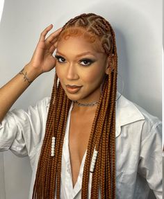 a woman with long braids is posing in front of a white wall and has her hand on her head