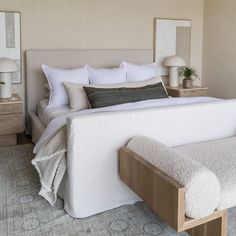 a bed with white linens and pillows in a neutral colored bedroom, along with two lamps on either side of the bed