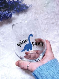 a person holding a wine glass with the word mine savy on it in front of purple flowers