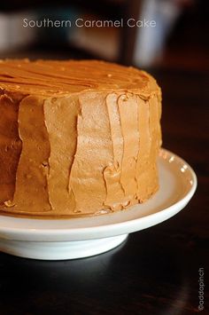 a frosted cake sitting on top of a white plate next to a wooden table