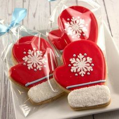 three heart shaped cookies with white frosting and snowflakes on them, sitting on a plate