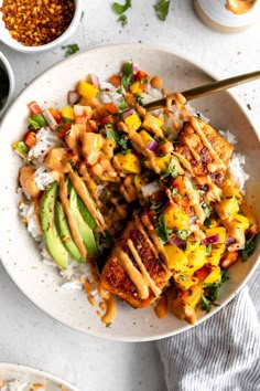 a white plate topped with chicken and rice covered in sauce next to bowls of vegetables