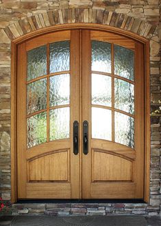 a pair of double doors with glass on the top and bottom, in front of a stone wall