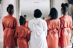 four women in orange robes are looking at their reflection in a mirror and one is wearing a white robe