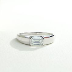 a white gold ring with an emerald cut diamond in the center on a plain surface