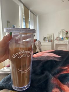 a person holding a cup with coffee in it on top of a bed next to a window