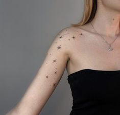 a woman wearing a black dress with stars on her left arm and shoulder, in front of a gray background