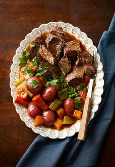 a white plate topped with meat and vegetables next to a fork on top of a blue napkin