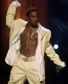 a man with no shirt on standing in front of a microphone and wearing a white suit