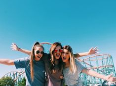 three girls are posing for the camera in front of a roller coaster