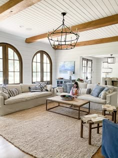 a woman sitting on a couch in a living room next to two large arched windows