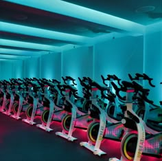 a row of stationary exercise bikes in a room with neon lights on the walls and floor