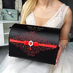 a woman in a wedding dress holding a black box with a red bow on it