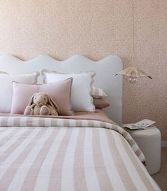 a teddy bear sitting on top of a bed with pink and white pillows in a bedroom