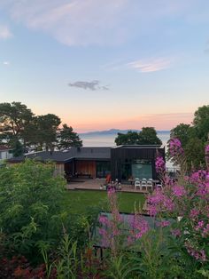 the house is surrounded by purple flowers and greenery, with an ocean view in the background