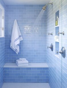 a bathroom with blue tiles and white towels on the shelf next to the bathtub