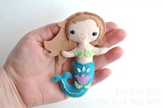 a hand holding a small felt doll in it's right hand, with the little mermaid on top