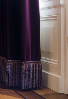 a cat sitting on the floor in front of a window with purple curtains behind it