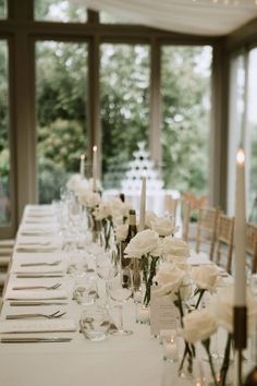 a long table is set with white flowers and candles for an elegant wedding reception in front of large windows