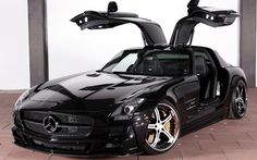 a black mercedes sls with its doors open and the hood up is parked in front of a white wall