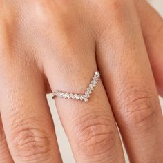 a woman's hand with a diamond ring on top of her finger and an arrow shaped band