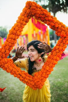 a woman in yellow dress holding up an orange frame with flowers around her neck and hands