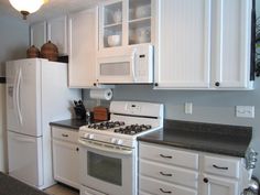 a kitchen with white cabinets and black counter tops, including a stove top oven and refrigerator