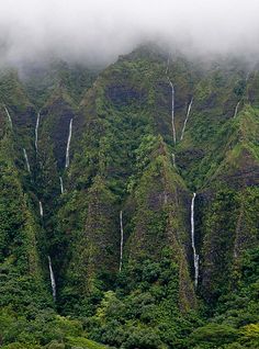 the mountains are covered in green vegetation and waterfall cascadings, while fog hangs over them