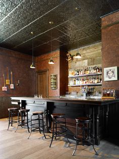 a bar with several stools and bottles on the shelves in front of it,