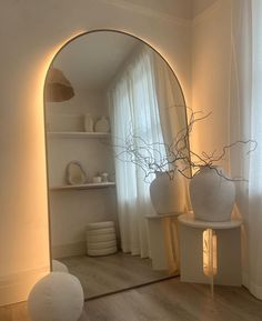 a mirror sitting on top of a wooden floor next to a white vase and shelf