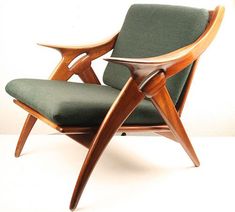 a wooden chair with green upholstered seat and arm rests against a white wall