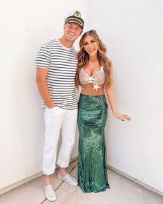 a man standing next to a woman in a green mermaid skirt and white sailor's hat