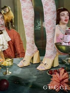 a woman's legs in high heels sitting at a table next to a cake