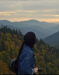 a person standing on top of a hill with a camera in hand and mountains in the background