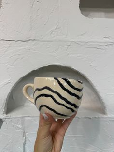 a hand holding a coffee cup in front of a white wall with black lines on it