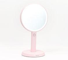 a pink mirror sitting on top of a white table next to a wall mounted light