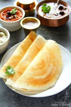 two pita breads on a white plate with dipping sauces in bowls behind them