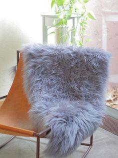 a chair with a fur pillow on it in front of a window and a potted plant