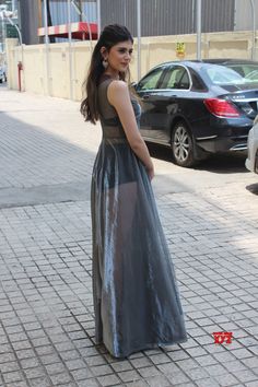 a woman in a long dress standing on the sidewalk