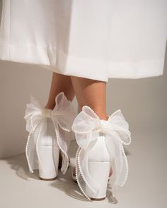 a woman's feet wearing white high heels with bows