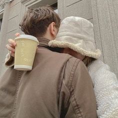 a man and woman hugging each other with a cup of coffee in their hand while standing next to a building