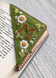 an open book with a piece of felt on top of it and some daisies