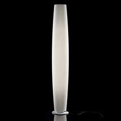 a tall white vase sitting on top of a black table next to a light bulb