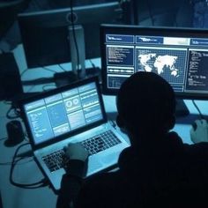 a man sitting in front of two computer monitors on top of a desk next to a laptop