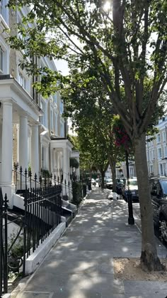 a row of white townhouses with black iron fence and trees on the sidewalk in front of them