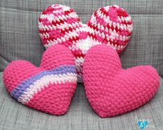 three pink crocheted hearts sitting on top of a gray couch next to each other