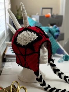 a knitted spiderman hat on top of a white headpiece next to scissors