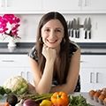 a woman sitting in front of a table full of fruits and vegetables, smiling at the camera